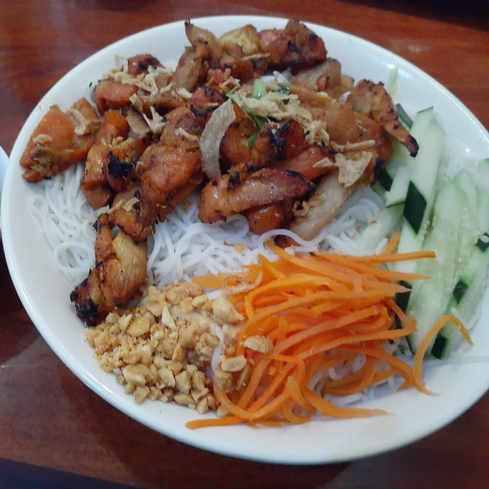 A Vietnamese vermicelli bowl with grilled chicken, peanuts, shredded carrots, and cucumber slices.