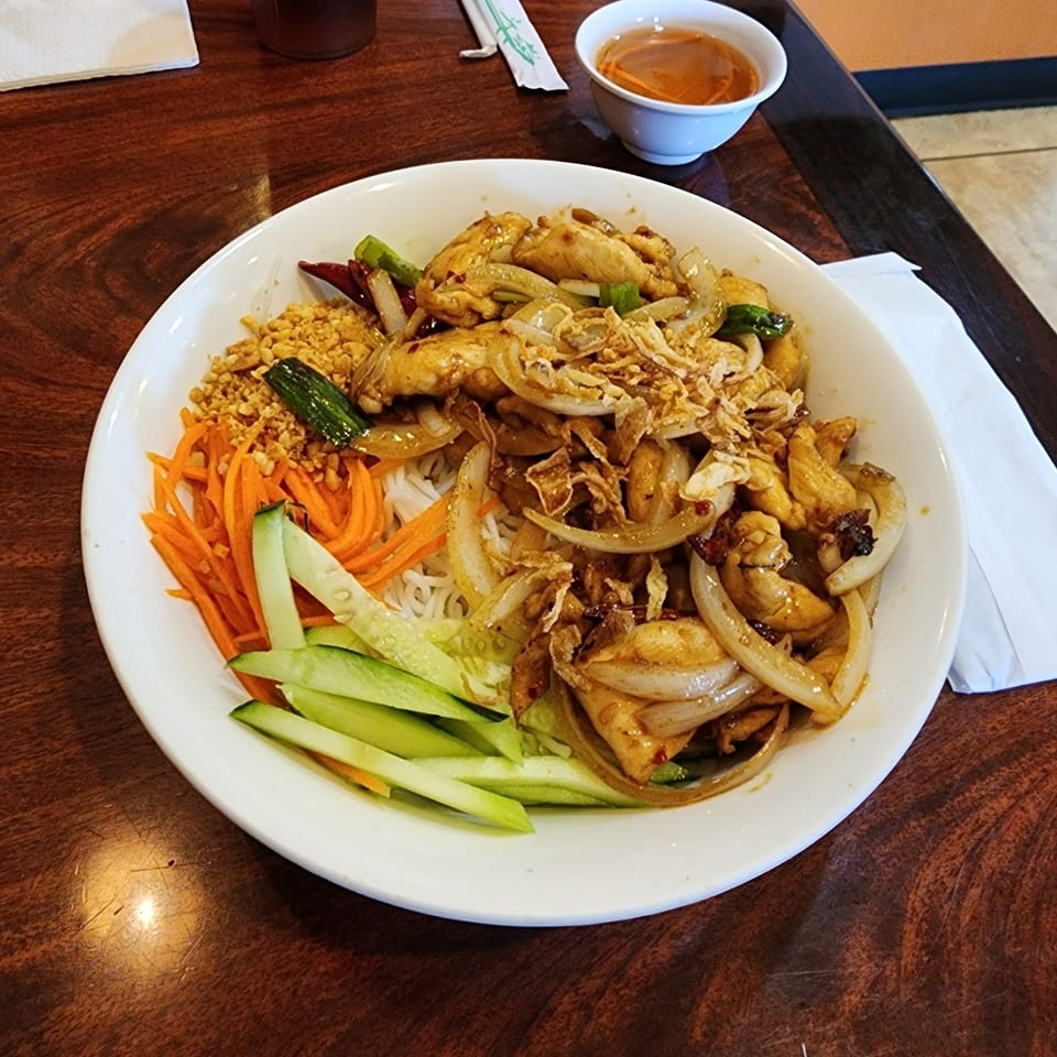 A Vietnamese vermicelli bowl with chicken, onions, peanuts, carrots, and cucumbers on a wooden table.