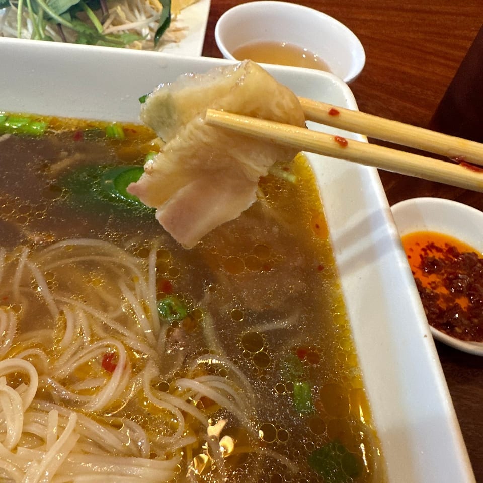 Chopsticks holding a piece of meat above a bowl of Pho Hung Cuong's Vietnamese pho.