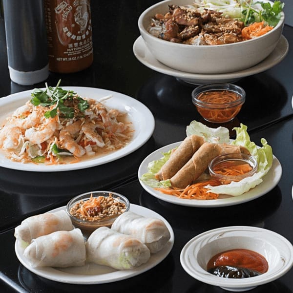 A table spread of Vietnamese dishes including shrimp salad, spring rolls, and a noodle bowl.