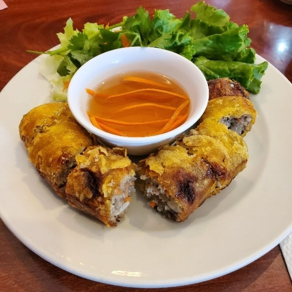 Crispy Vietnamese fried spring rolls, one cut open, with lettuce and a dipping sauce on a white plate.