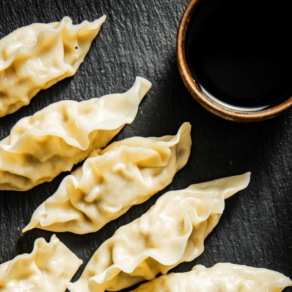 Steamed Vietnamese dumplings arranged on a dark slate surface, with a small bowl of soy sauce.