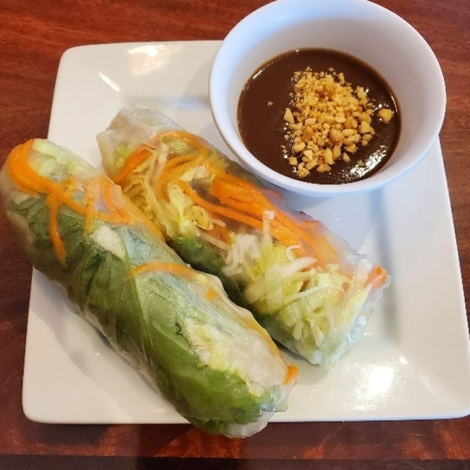 Two fresh Vietnamese spring rolls with vegetables and shrimp, served with a peanut dipping sauce.