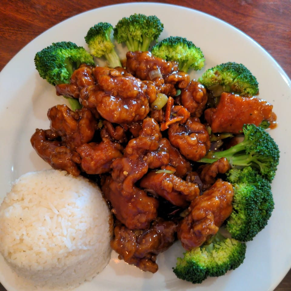 Sweet and sour chicken with broccoli and white rice on a white plate.
