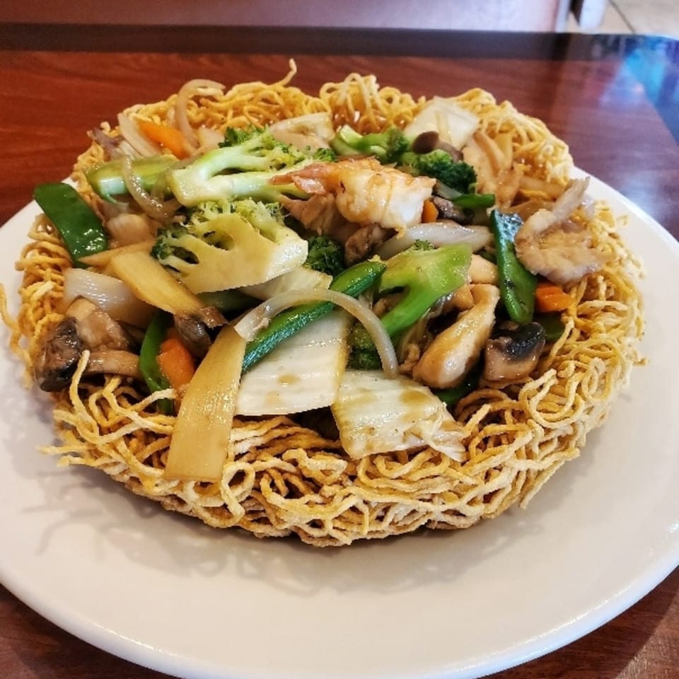 Crispy Vietnamese egg noodles topped with stir-fried shrimp, chicken, and mixed vegetables on a white plate.