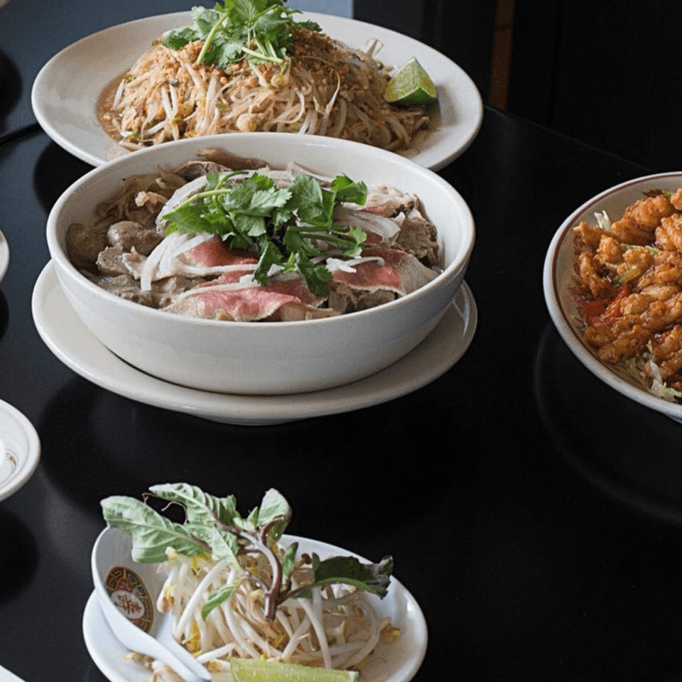 A table spread of Vietnamese dishes, including pho, noodles, and a side of bean sprouts.